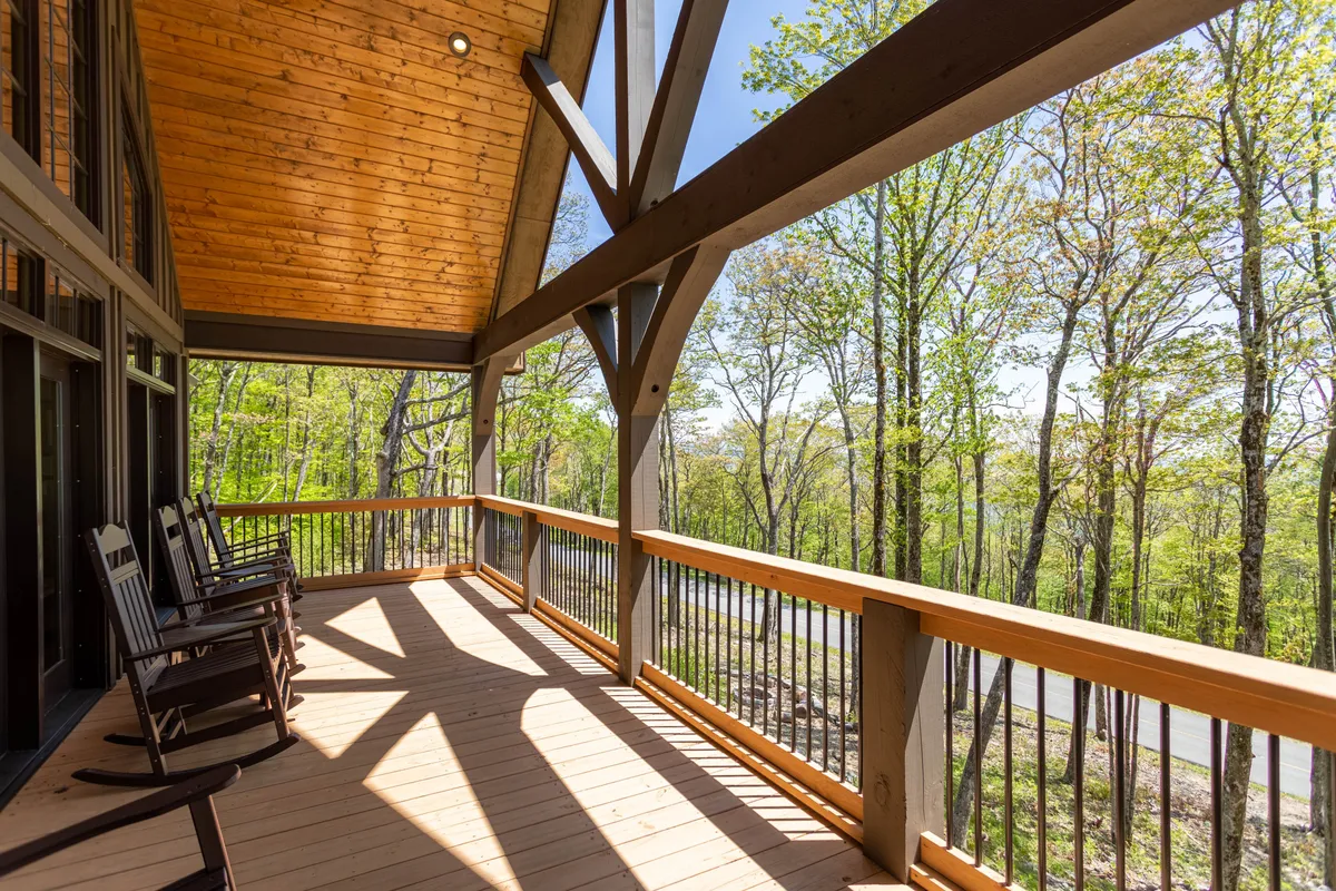 A cozy porch with classic wooden rocking chairs and a wooden railing overlooks a forested landscape. The setting encourages relaxation, morning coffees, and enjoying mountain air and privacy—key aspects of the lodge’s luxury experience.