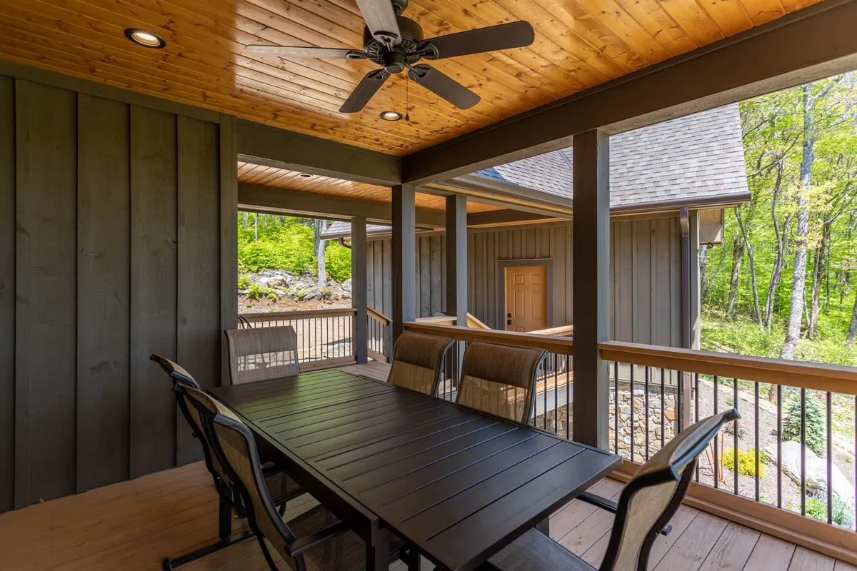 An inviting outdoor dining space with a wooden table, ceiling fan, and lush greenery in the background. The setting is designed for group meals, celebrations, and enjoying nature together. The covered patio suggests flexibility for both daytime and evening gatherings, with plenty of space to host friends or family.