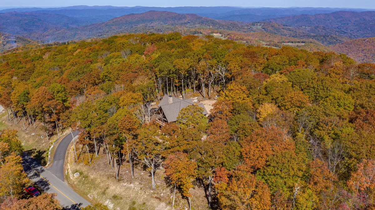 This image captures the lodge nestled amid tall trees, with a winding road leading toward distant mountains. The surrounding forest and the open sky evoke a deep sense of immersion in nature, suggesting immediate access to hiking and biking trails.