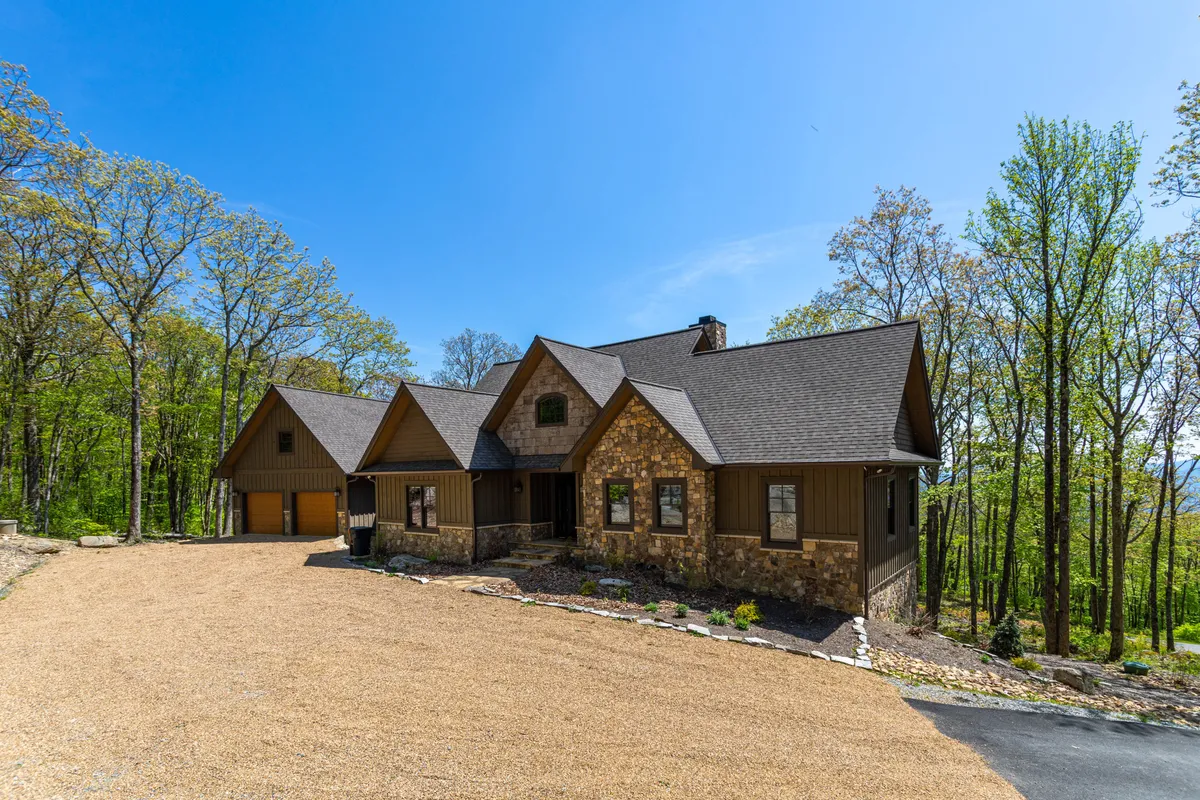 A broad view of the main entrance of Papa Bear Lodge, featuring its impressive stone facade, roofline, and tree-filled surroundings. The scene sets a tranquil and inviting mood, hinting at the spaciousness inside and the lodge’s connection to nature.