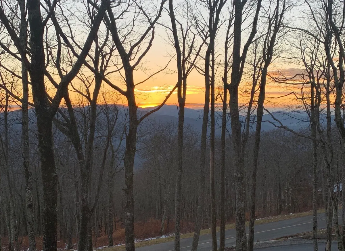 A breathtaking sunset stretches over a mountain range, with tree silhouettes in the foreground. The soft, colorful sky conveys a peaceful end to an adventurous day outdoors, aligning with mentions of sunset views and nature appreciation.