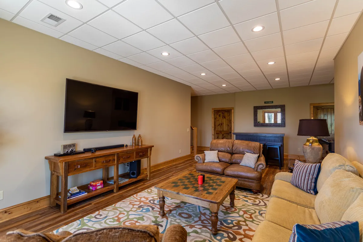 A spacious, comfortable lounge area is anchored by a large flat-screen TV, plush leather sofas, a colorful area rug, and a wooden coffee table, ideal for movie nights or group relaxation.