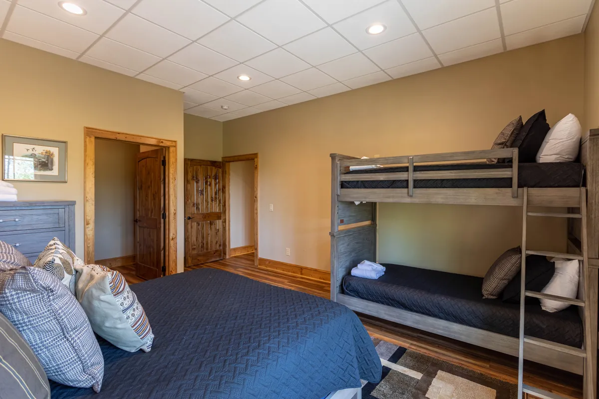 A flexible family suite with a comfortable double bed and a colorful bunk bed, wood trim and doors, and playful decorative pillows—ideal for kids or groups seeking both comfort and togetherness.